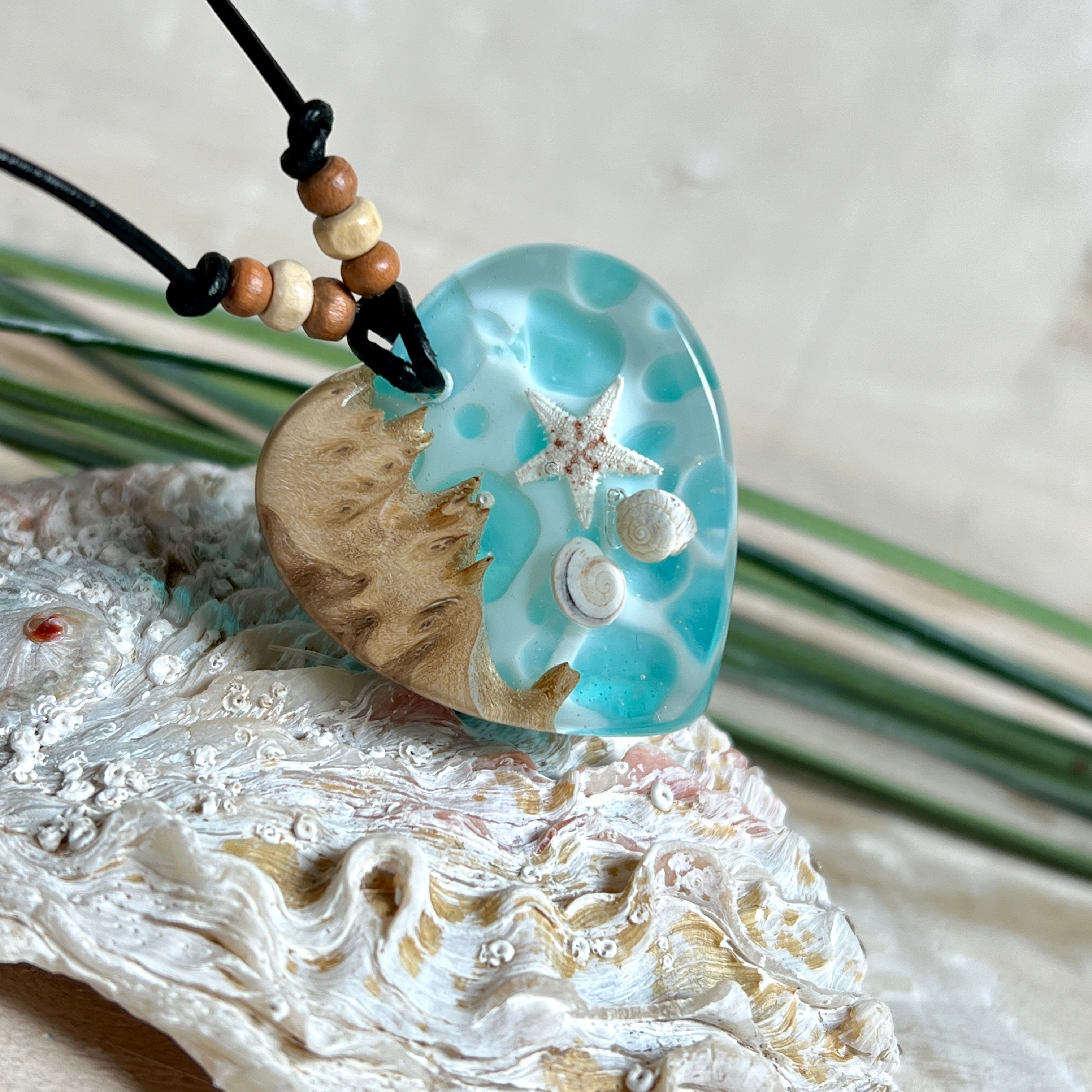 Handgefertigter Herzanhänger aus Maserholz und transparentem Ocean-Harz mit echtem Seestern und Muscheln. Die zarten Aqua-Farben erinnern an Meereswellen. Lederband verstellbar mit Holzperlen. Größe ca. 3,5 × 3,2 cm. Natürliches, maritimes Unikat von ZeitlosSchmuckDesign