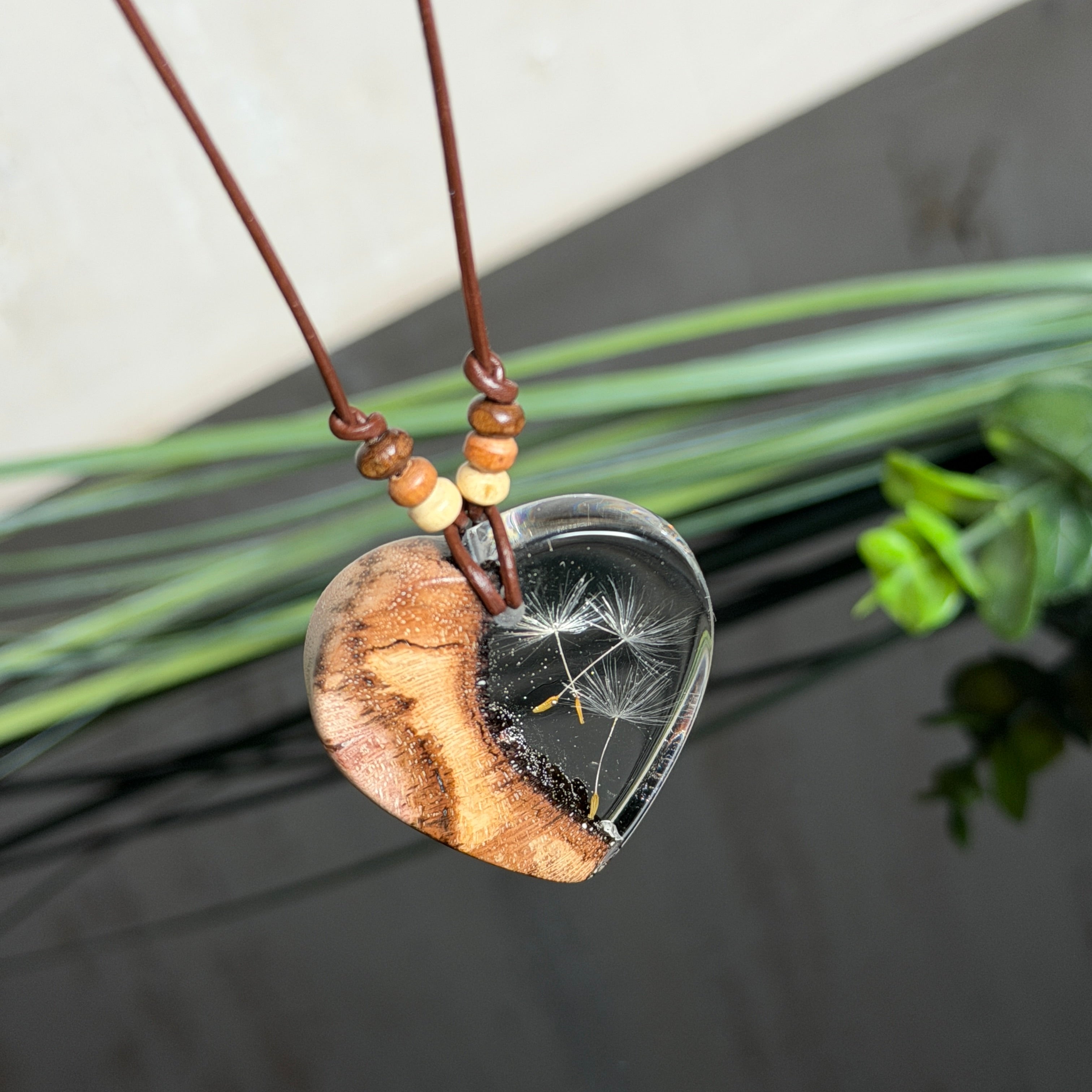 Herzanhänger „Pusteblumenzauber“ aus naturbelassenem Rebholz und klarem Epoxidharz mit schwebenden Pusteblumensamen. Dunkelbraunes, verstellbares Lederband mit kleinen Holzperlen, Anhänger ca. 3,5 × 3,5 cm. Handgefertigtes Unikat von ZeitlosSchmuckDesign.