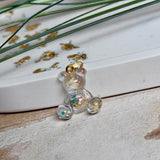 Kleiner Bärchen-Anhänger aus transparentem Harz mit irisierenden Flakes in Regenbogen-Schimmer, goldfarbene Anhängerschlaufe aus Edelstahl. Größe ca. 2,2 × 2,1 cm. Handgefertigtes Unikat; Flakes-Anordnung variiert, vereinzelt kleine Luftbläschen möglich.