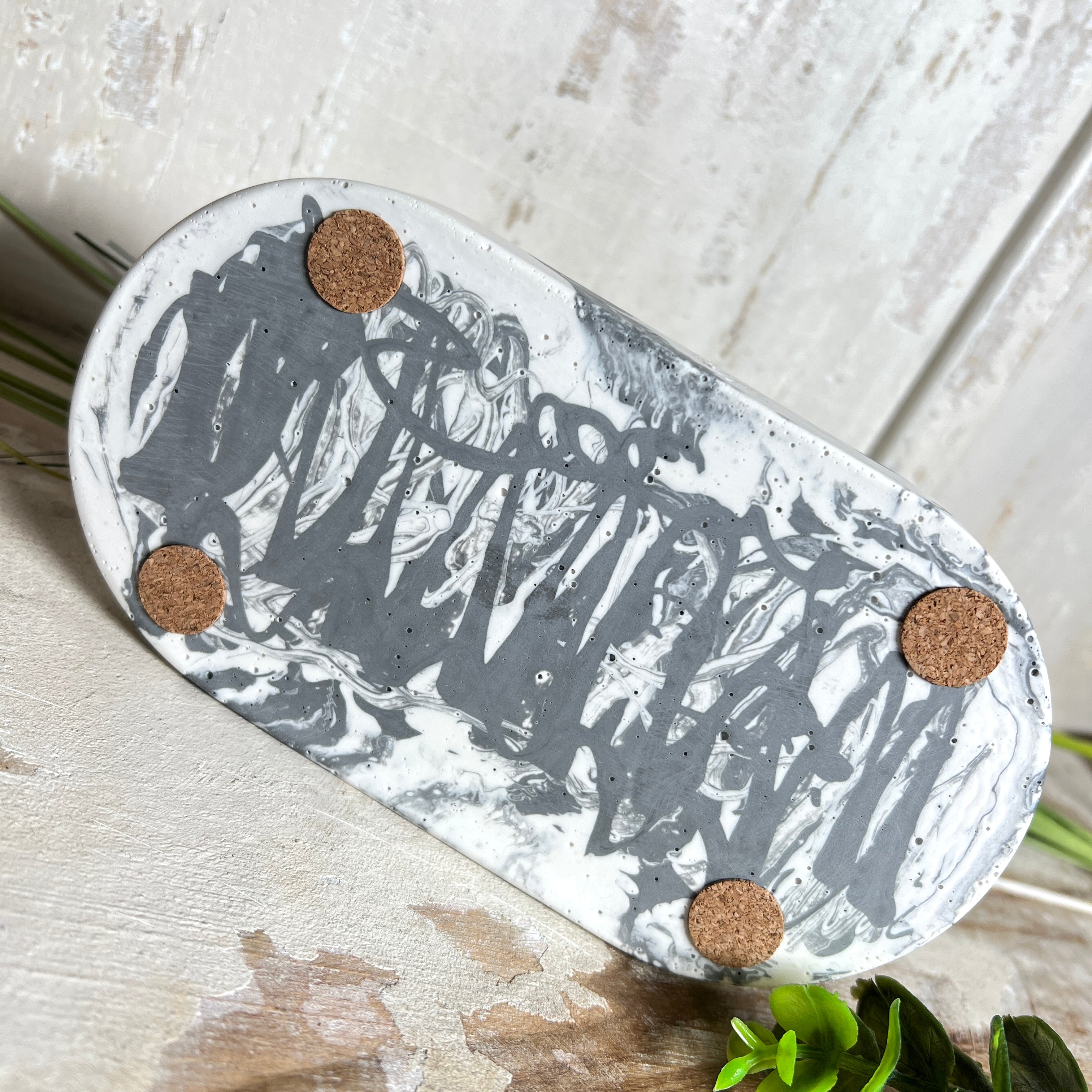 Handgegossenes Schmucktablett aus Jesmonite mit grau -weißer Marmorierung. Die ovale Form und die individuelle Musterung machen jedes Stück einzigartig. Die Rückseite ist mit rutschfesten Korkpunkten ausgestattet – ideal als stilvolle Ablage für Schmuck, Kristalle, Schlüssel oder Brille. Unikat in modernem Monochrom-Design. Lieferung ohne Deko.