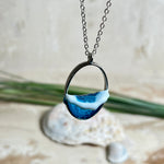 Ovale Halskette „Ocean Crest“ mit 3D-Welle: handgefertigter Harz-Anhänger in Silber-Legierung, Farbverlauf von Tiefblau zu Türkis mit weißer Schaumkrone. Größe ca. 3,9 × 2,3 cm, an einer ca. 56 cm langen versilberten Kette. Glänzende Oberfläche, maritimer Look, Unikat-Handarbeit.