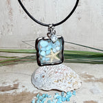 Quadratischer Larimar-Mosaik Anhänger im Edelstahlrahmen mit Seestern-Element und facettierter Bergkristall-Perle, eingebettet in Harz, an schwarzer Lederkette.