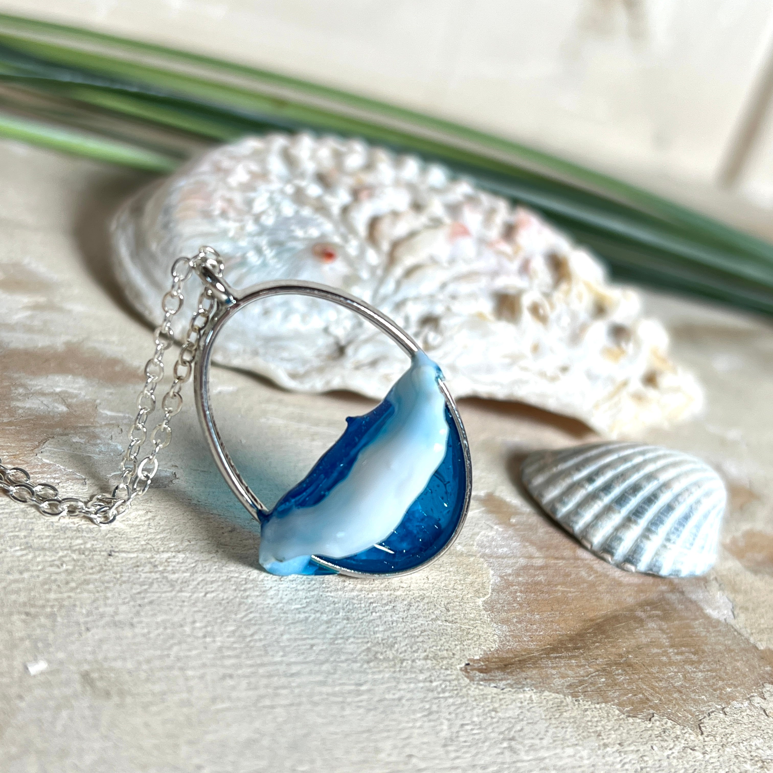 Ovale Halskette „Ocean Crest“ mit 3D-Welle: handgefertigter Harz-Anhänger in Silber-Legierung, Farbverlauf von Tiefblau zu Türkis mit weißer Schaumkrone. Größe ca. 3,9 × 2,3 cm, an einer ca. 56 cm langen versilberten Kette. Glänzende Oberfläche, maritimer Look, Unikat-Handarbeit.