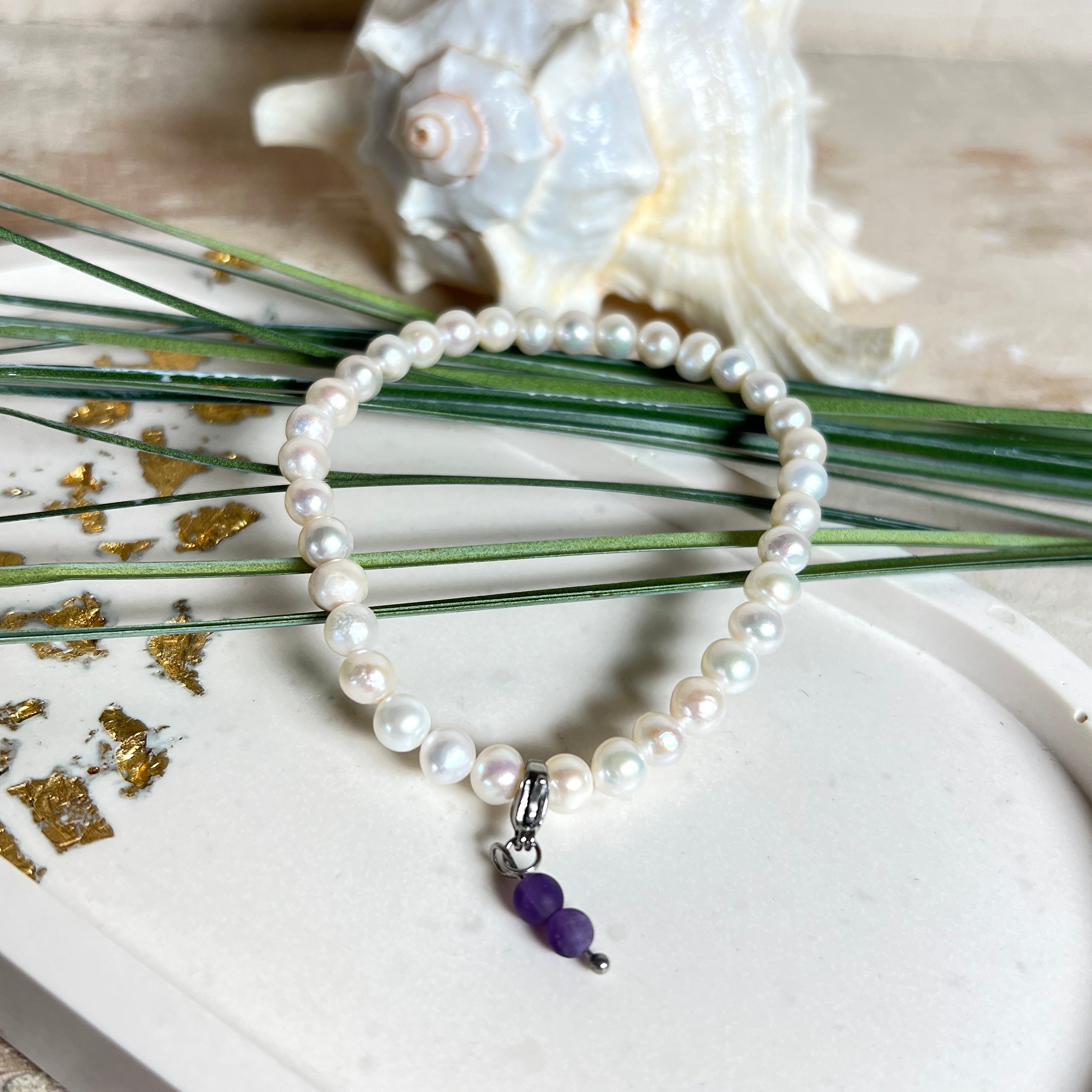 Handgefertigtes Armband „Sea Harmony“ mit schimmernden Süßwasserperlen (Ø ca. 6–7 mm), jede Perle ein Unikat. Auf elastischem Band gefädelt, mit einem filigranen Charmanhänger aus  Amethyst-Perlen, befestigt an einem robusten Edelstahl-Karabiner. Ein Schmuckstück voller Eleganz, maritimer Harmonie und symbolischer Tiefe – ideal als Geschenk oder als stilvolles Accessoire.