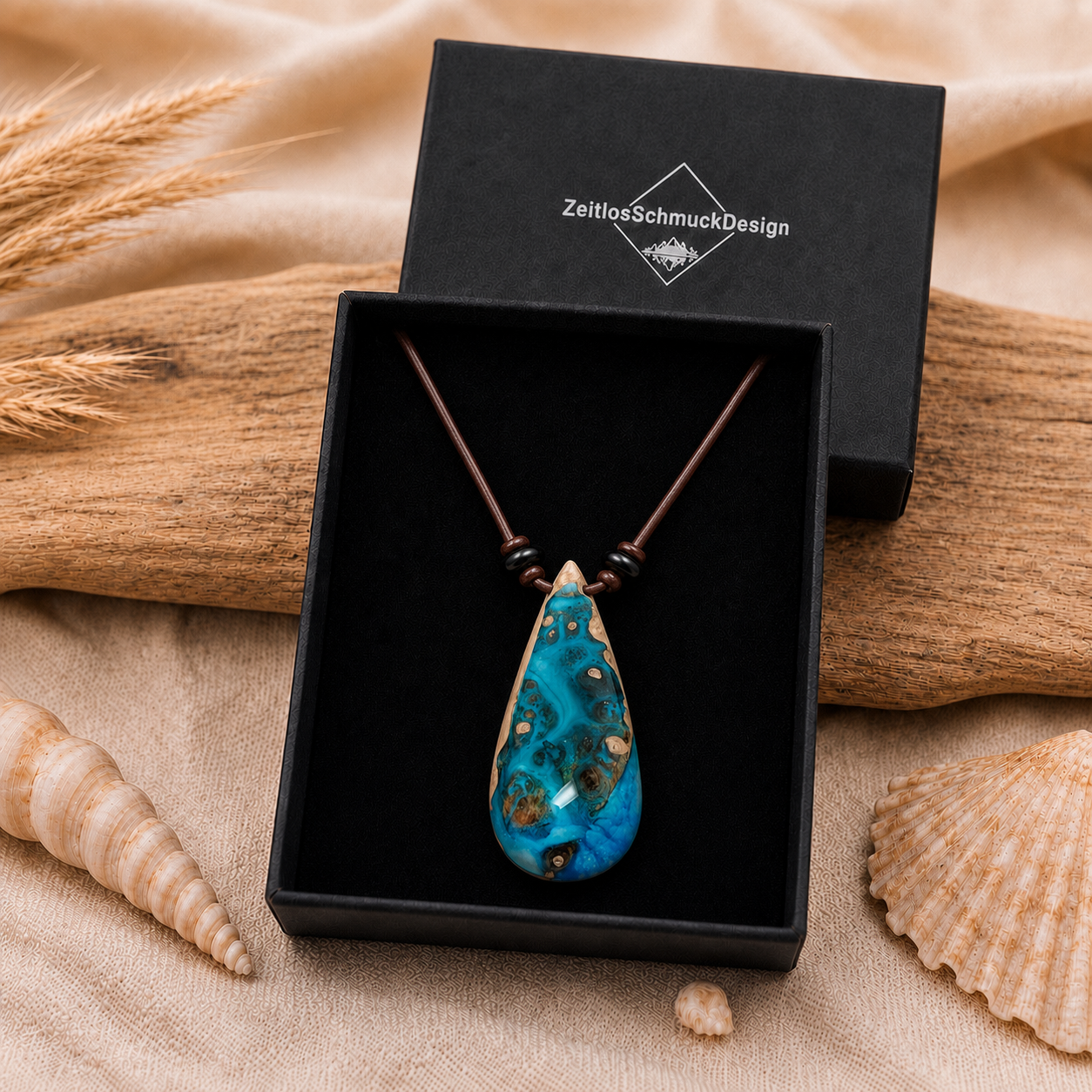 Schmuckbox-Bild KORALLENBUCHT – handgefertigter Holz-Harz-Anhänger aus Maserholz und türkis-blauem Epoxidharz, am braunen Lederband mit flachen Onyxperlen, präsentiert in schwarzer ZeitlosSchmuckDesign Schmuckbox, maritimer Naturschmuck als einzigartiges Unikat.