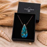 Schmuckbox-Bild KORALLENBUCHT – handgefertigter Holz-Harz-Anhänger aus Maserholz und türkis-blauem Epoxidharz, am braunen Lederband mit flachen Onyxperlen, präsentiert in schwarzer ZeitlosSchmuckDesign Schmuckbox, maritimer Naturschmuck als einzigartiges Unikat.