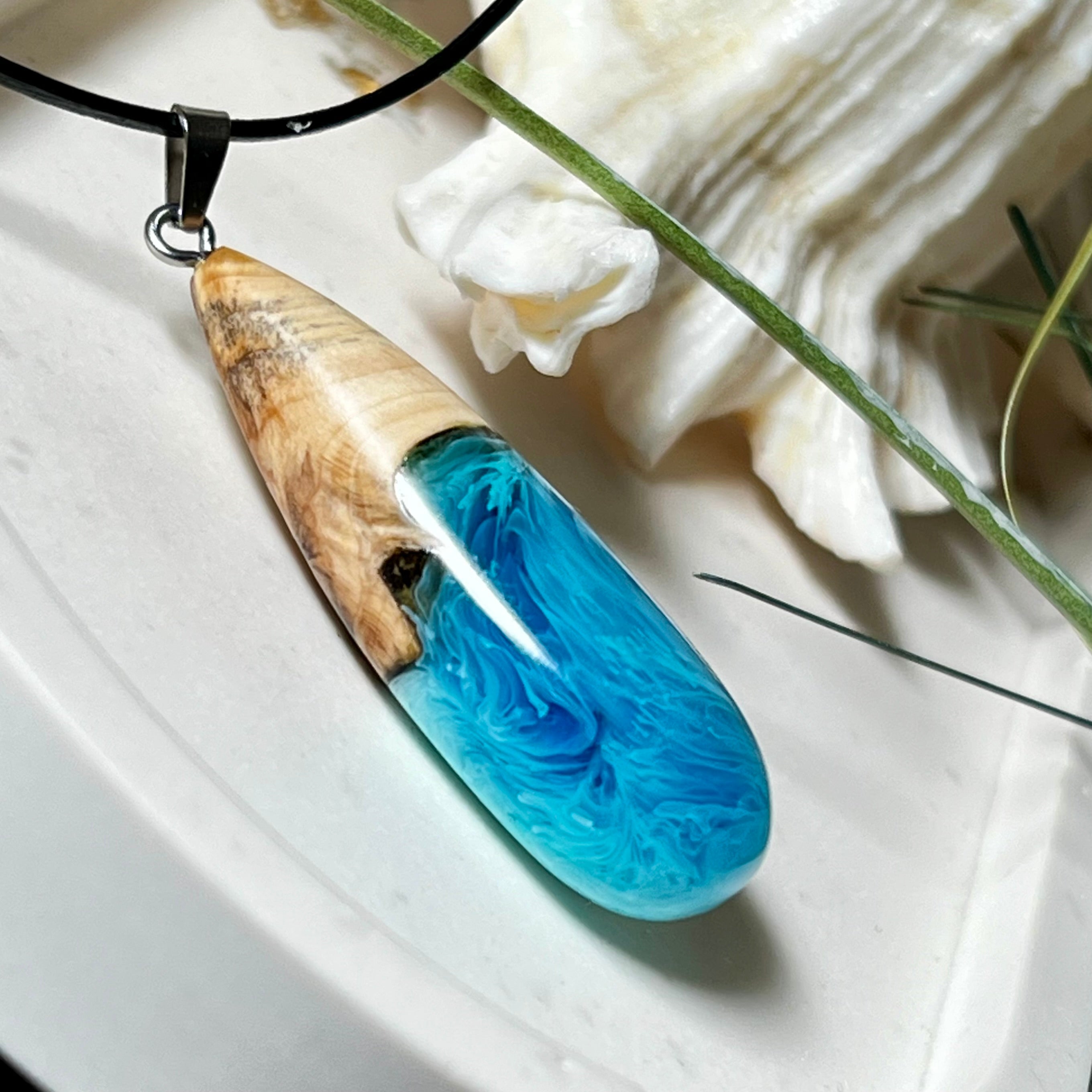 Tropfenförmiger Anhänger aus Maserholz und Harz in leuchtenden Blautönen und Weiß. Inspiriert vom Meer, in Handarbeit gegossen,gesägt, geschliffen und hochglanzpoliert. Mit verstellbarer Lederkette (45 + 5 cm) und Edelstahlkarabiner. Jeder Anhänger ist ein Unikat mit natürlicher Maserung. Ein maritimes Schmuckstück für Naturfreunde und alle, die das Wasser lieben.