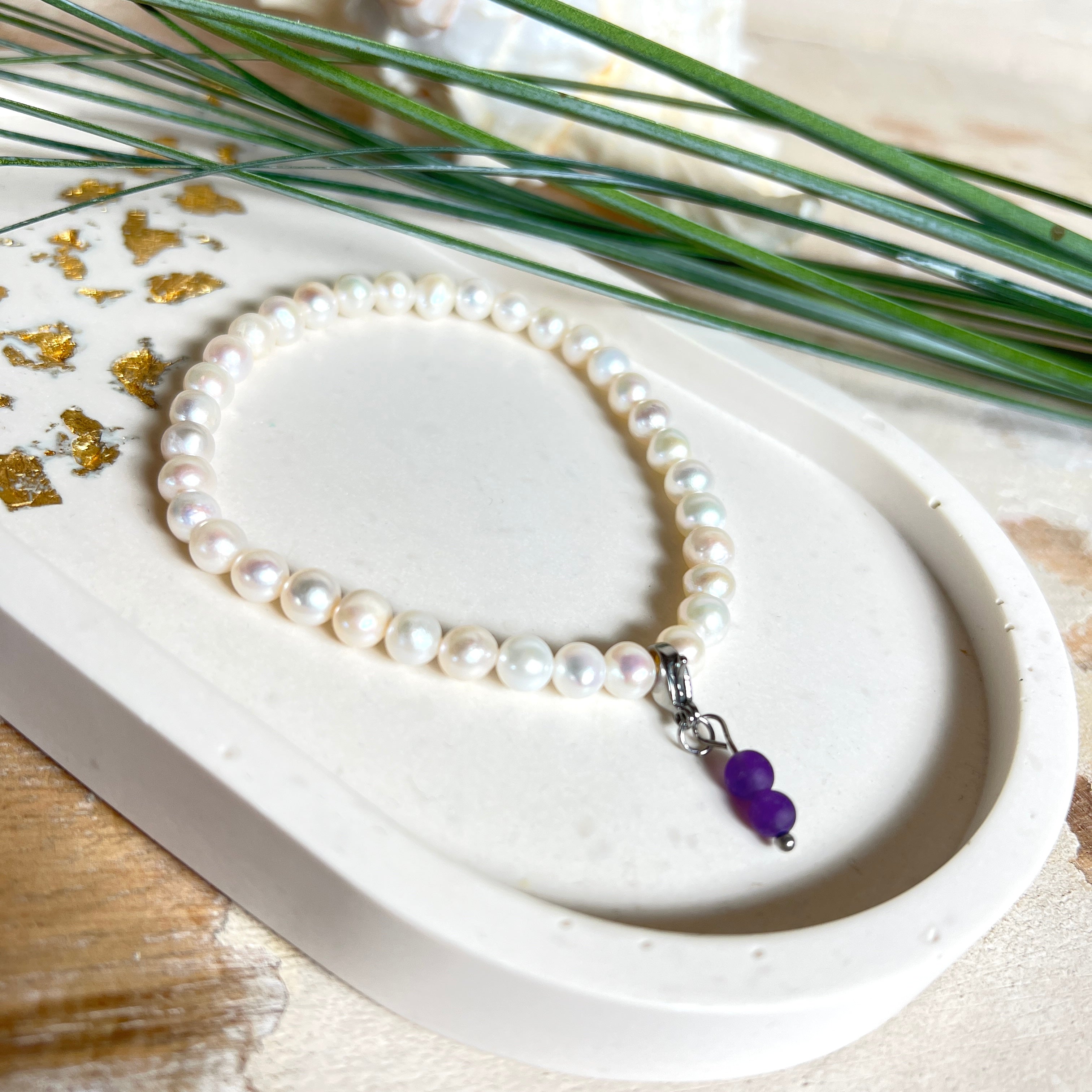 Handgefertigtes Armband „Sea Harmony“ mit schimmernden Süßwasserperlen (Ø ca. 6–7 mm), jede Perle ein Unikat. Auf elastischem Band gefädelt, mit einem filigranen Charmanhänger aus  Amethyst-Perlen, befestigt an einem robusten Edelstahl-Karabiner. Ein Schmuckstück voller Eleganz, maritimer Harmonie und symbolischer Tiefe – ideal als Geschenk oder als stilvolles Accessoire.