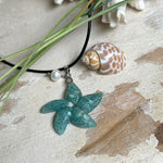 Seestern-Anhänger aus transparentem Harz mit echtem Meersand ( leicht eingefärbt), in blautürkis Strand-Look, mit kleiner Süßwasserperle als Anhänger-Detail. Edelstahlöse, schwarze Lederkette mit Edelstahl-Karabiner und Verlängerung (45 cm + 5 cm). Anhänger ca. 3,5 × 3,5 cm. Handgefertigtes Unikat; vereinzelt kleine Luftbläschen möglich, typisch für Handarbeit.