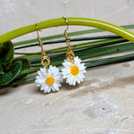 Handgefertigte Gänseblümchen-Ohrringe aus Harz mit 925 vergoldeten Ohrhaken, weiße Blüte mit gelbem Zentrum, goldfarbene Details, Länge ca. 4,5 cm.
