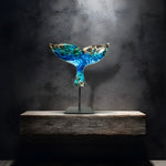 Handgefertigte Walflossen-Skulptur „Ocean Grace“ aus Maserholz und Epoxidharz in Blau, Weiß und Türkis, auf schwarzem Metallständer, ca. 29 x 27 cm, als exklusives maritimes Deko-Kunstwerk auf einem modernen Sideboard vor dunkler Wand platziert.