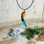 Handgefertigter Anhänger aus Edelholz und transparent-türkisblauem Epoxidharz, glatt poliert. Größe ca. 6,7 × 2,0 cm. Mit Edelstahlöse an schwarzer Lederkette (45 cm + 5 cm Edelstahl-Verlängerung, Karabiner). Maritimer, moderner Unisex-Schmuck mit natürlicher Holzmaserung; kleine Lufteinschlüsse sind charakteristisch.