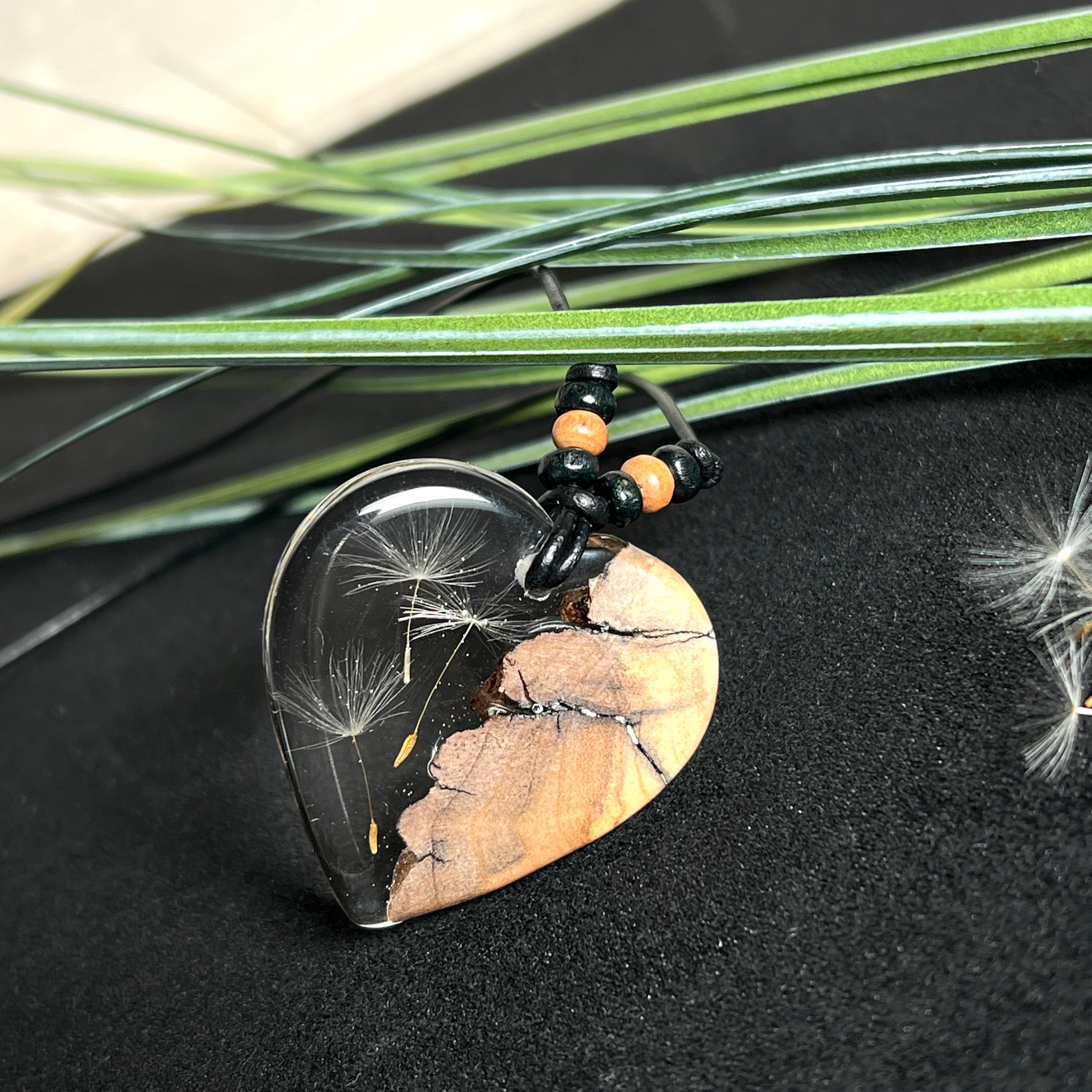 „Handgefertigter Herzanhänger aus Olivenholz und klarem Harz mit echter Pusteblume. Der Anhänger (ca. 3,5 × 3,5 cm) hängt an einem verstellbaren Lederband (23–43 cm) mit Holzperlen. Symbol für Wünsche und Glück, sorgfältig in Handarbeit gegossen, gesägt, geschliffen und poliert. Ein einzigartiger, naturinspirierter Anhänger – ideal als Geschenk oder persönlicher Talisman.“