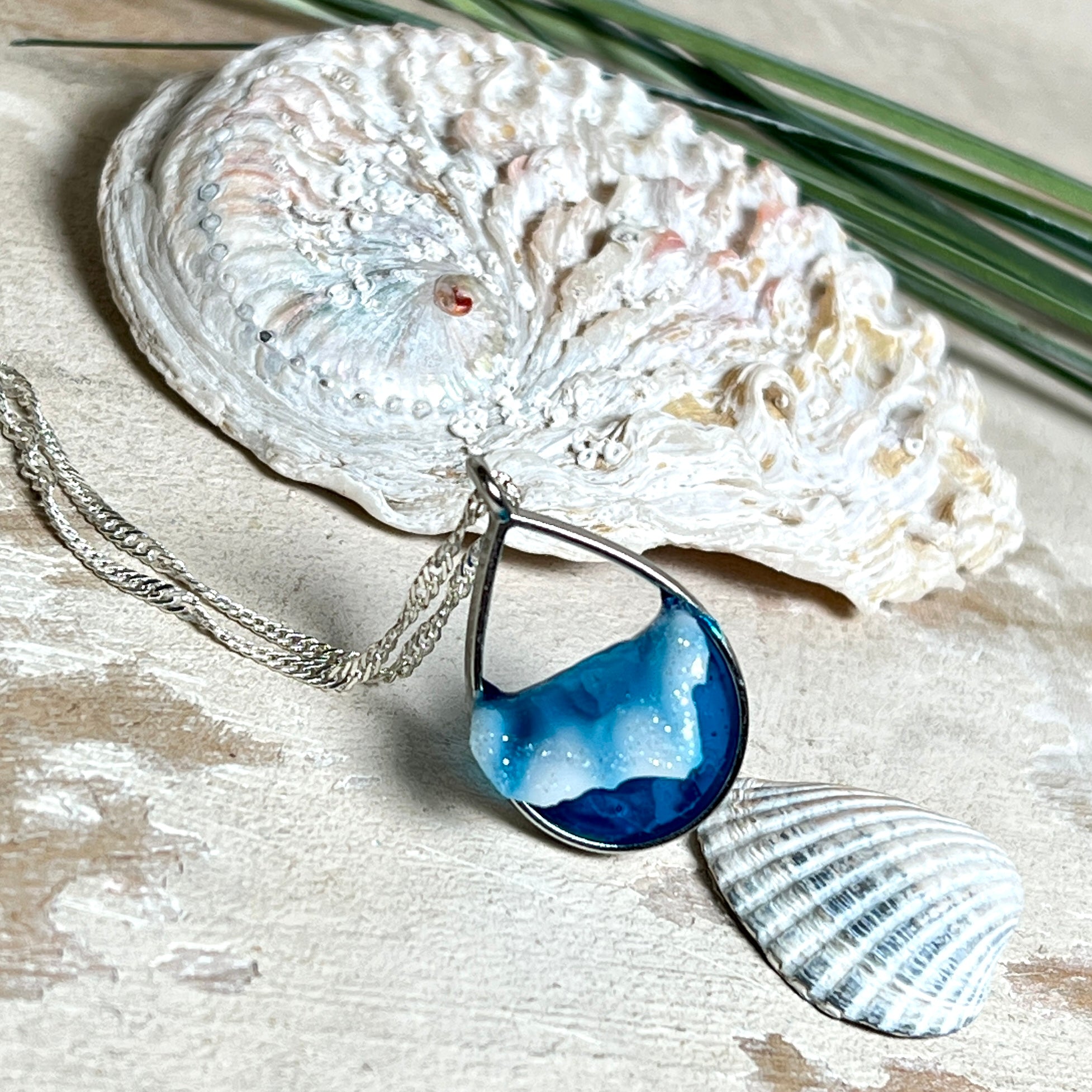 „Lagunenlicht“ – Tropfenanhänger mit handmodellierter 3D-Welle und feinem Glitzereffekt. Klarer Harzlook in Blau/Türkis, gefasst in Silber-Legierung. Größe ca. 3,5 × 2 cm. Geliefert an einer versilberten Kette (ca. 56 cm). Hochglänzend , maritimer Unikatcharakter.