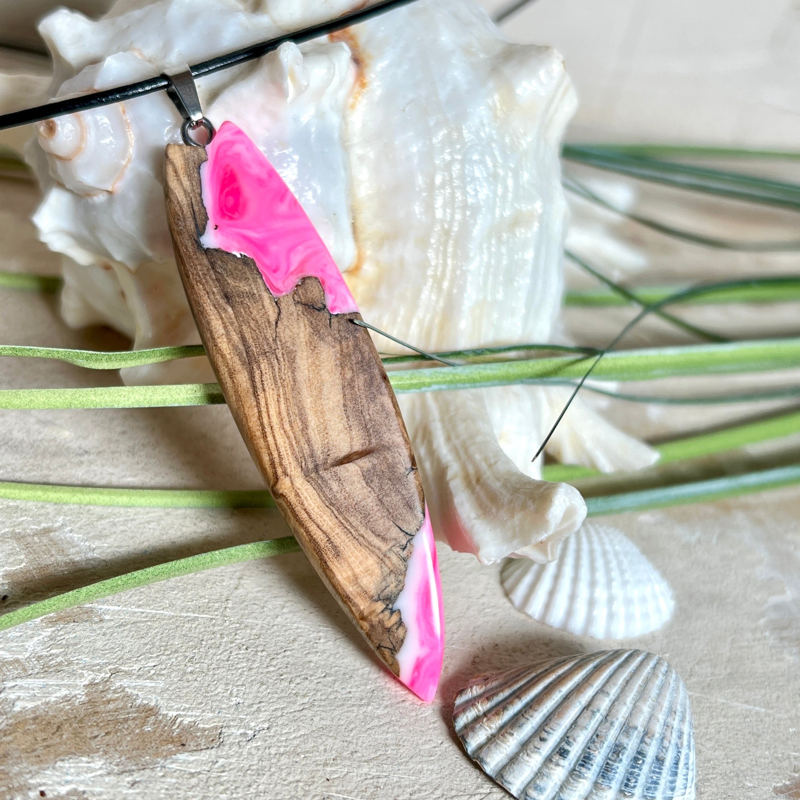 Handgefertigter Surfbrett-Anhänger „Pink Glow“ aus edlem Olivenholz und fluoreszierendem Epoxidharz in Pink & Weiß. Fluoreszierend bei Schwarzlicht, mit Edelstahl-Anhängerschlaufe und schwarzer Lederkette (45 cm + 5 cm Verlängerung). Ein maritimes Unikat – perfekt als Geschenk für Surfer und Meeresliebhaber.