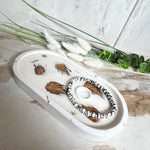 Handgefertigtes Schmucktablett aus Jesmonite mit echten Zapfen, die in einer glänzenden Resin-Schicht eingebettet sind. Die ovale Form und die natürliche Farbgebung machen es zu einem stilvollen Wohnaccessoire. Mit rutschfesten Korkpunkten auf der Unterseite ideal als Ablage für Schmuck, Schlüssel oder Dekoartikel. Jeder Artikel ist ein Unikat aus Handarbeit – Lieferung ohne Dekoration.