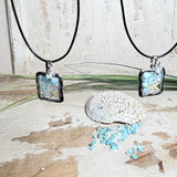 Quadratischer Larimar-Mosaik Anhänger im Edelstahlrahmen mit Seestern-Element und facettierter Bergkristall-Perle, eingebettet in Harz, an schwarzer Lederkette.