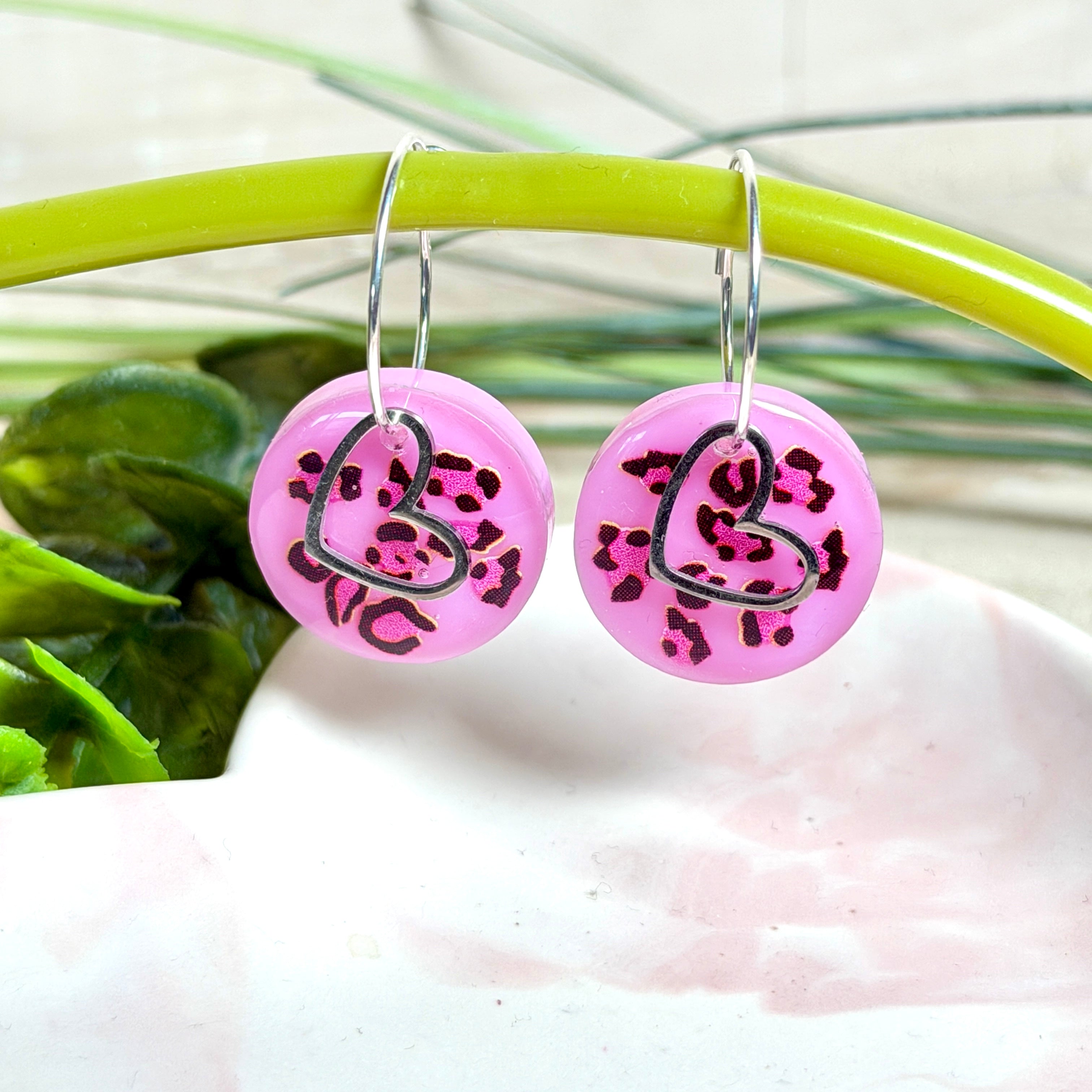 Handgemachte Leo-Creolen aus 925 Silber: Silber-Creolen 16 mm mit rosa Harz-Scheibe (2 cm) im Leoparden-Look und Edelstahl-Herzanhänger. Hängende Ohrringe in Animal-Print Stil, Gesamtlänge ca. 3,5 cm. Resin-Ohrringe für Alltag, Party oder Festival, femininer Statement-Schmuck in Rosa/Pink mit silberfarbenen Metallteilen. Einzeln gegossen, jedes Paar ein Unikat; leichte Abweichungen im Muster, Farbspiel und kleine Luftbläschen sind möglich und typisch für Handarbeit.