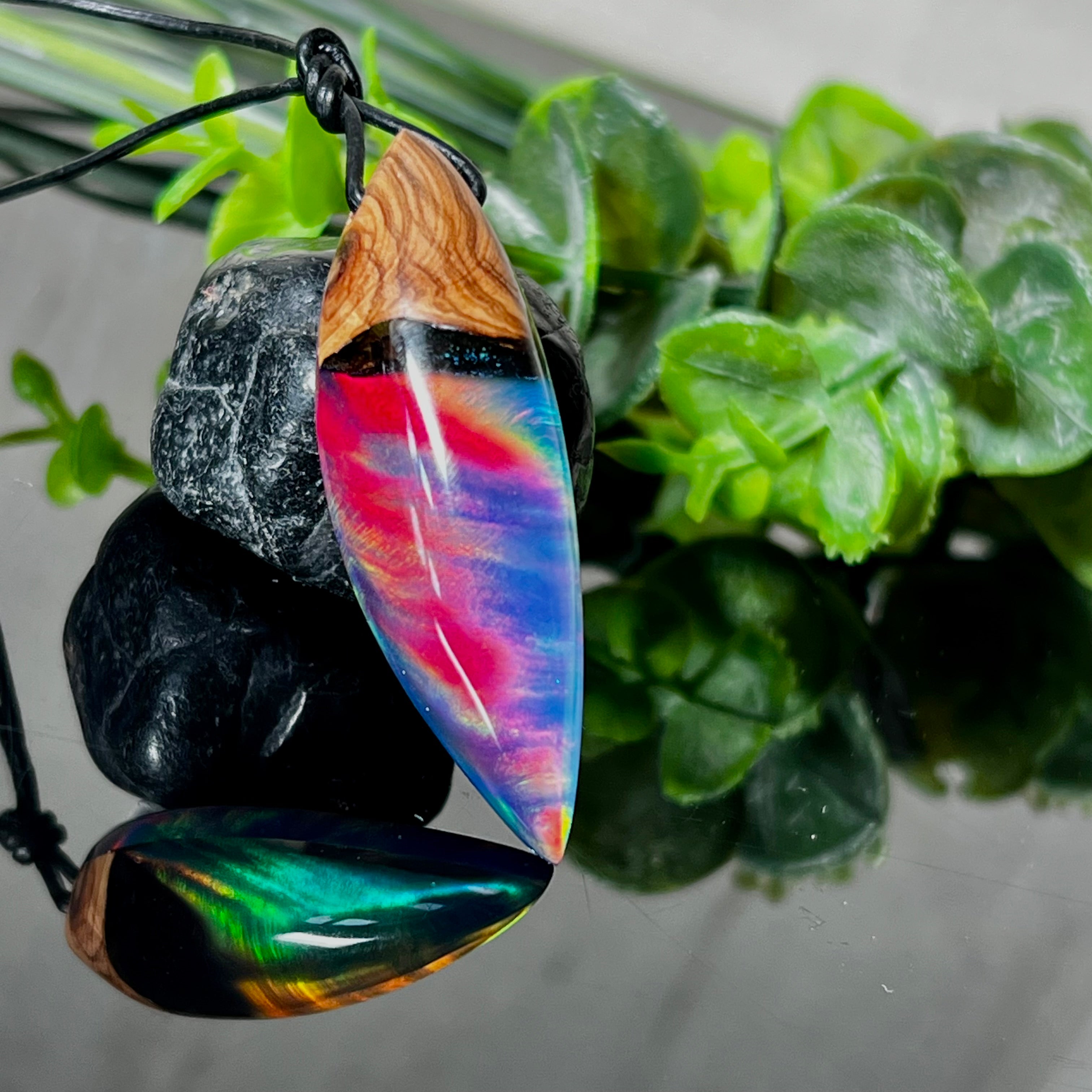 Der handgefertigte Anhänger „Celestial Flame“ kombiniert warmes Olivenholz mit glasklarem Harz und irisierendem Opal. Das einzigartige Farbspiel erinnert an Polarlichter und verleiht dem Schmuckstück eine mystische Tiefe. Die Oberfläche ist glatt poliert, der Anhänger wird an einem verstellbaren Lederband getragen – ein ausdrucksstarkes Unikat für alle, die Naturmaterialien und kreative Farben lieben.