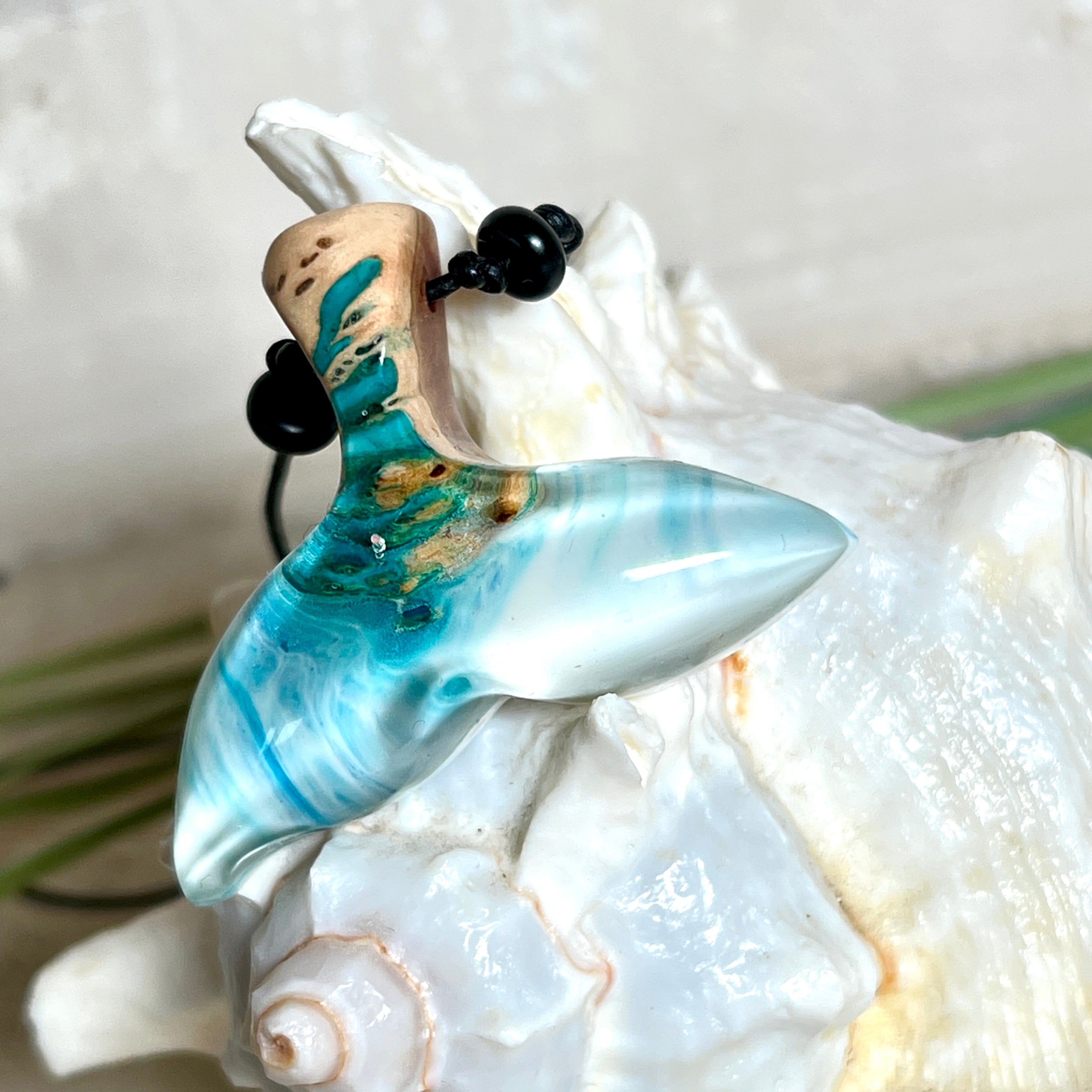 Walflossen-Anhänger „Flossenklang“ – handgefertigtes Unikat aus Maserholz und blau-weißem Harz. Die elegant geschwungene Form erinnert an die Flosse eines Wals und symbolisiert Freiheit, Stärke und Naturverbundenheit. Mit verstellbarem schwarzen Lederband und Onyxperlen gefertigt, ist jedes Stück ein individuelles Schmuckstück für Meeresliebhaber und Natursuchende. Maritimer Halsschmuck, inspiriert vom Ozean, glatt poliert und mit Liebe zum Detail von Hand gearbeitet.