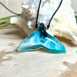 Walflossen-Anhänger „Flossenklang“ – handgefertigtes Unikat aus Maserholz und türkis-blau-grauen und weißem Harz. Die elegant geschwungene Form erinnert an die Flosse eines Wals und symbolisiert Freiheit, Stärke und Naturverbundenheit. Mit verstellbarem braunem Lederband gefertigt, ist jedes Stück ein individuelles Schmuckstück für Meeresliebhaber und Natursuchende. Maritimer Halsschmuck, inspiriert vom Ozean, glatt poliert und mit Liebe zum Detail von Hand gearbeitet.