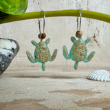 Türkisfarbene Schildkröten-Creolen an feinen 16-mm-Ringen aus 925 Silber, jeweils mit echtem Strandsand im Harz eingebettet und mit kleinen Jaspis-Edelsteinperlen verziert; handgefertigtes Unikat mit sommerlich-maritimem Look, fotografiert als Freisteller, Nahaufnahme oder auf dekorativem Untergrund.