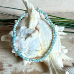 Zartes Larimar-Armband „Lagunenlicht“ mit facettierten 3 mm Perlen aus seltenem Atlantisstein auf Elastikfaden. Die kleinen Larimarsteine zeigen sanfte Blau- und Weißtöne wie Lagunenwasser. Innenumfang ca. 19 cm. Fotografiert auf Muscheln, einem dekorativen Stein und in einer schwarzen Schmuckbox von ZeitlosSchmuckDesign im maritimen Stil.
