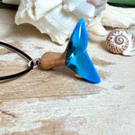 Handgefertigter Walflossen-Anhänger aus Olivenholz und Epoxidharz in Blau-Grün-Weiß, polierte Oberfläche, Edelstahl-Öse. Schwarze Lederkette 45 cm mit Edelstahl-Karabinerverschluss und 5 cm Edelstahl-Verlängerung. Anhängergröße ca. 2,5 × 3,2 cm, maritime Produktfotografie.