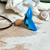 Handgefertigter Walflossen-Anhänger aus Olivenholz und Epoxidharz in Blau-Grün-Weiß, polierte Oberfläche, Edelstahl-Öse. Schwarze Lederkette 45 cm mit Edelstahl-Karabinerverschluss und 5 cm Edelstahl-Verlängerung. Anhängergröße ca. 2,5 × 3,2 cm, maritime Produktfotografie.