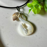 Detailaufnahme eines handgefertigten Anhängers aus echtem Perlmutt in Schlaufenform, kombiniert mit einer kleinen echten Muschel als Charm-Anhänger. Der Schmuck hängt an einer feinen schwarzen Lederschnur mit Edelstahlverschluss und symbolisiert Harmonie und Unendlichkeit. Ideal für Meeresliebhaberinnen und Fans von Naturmaterialien.