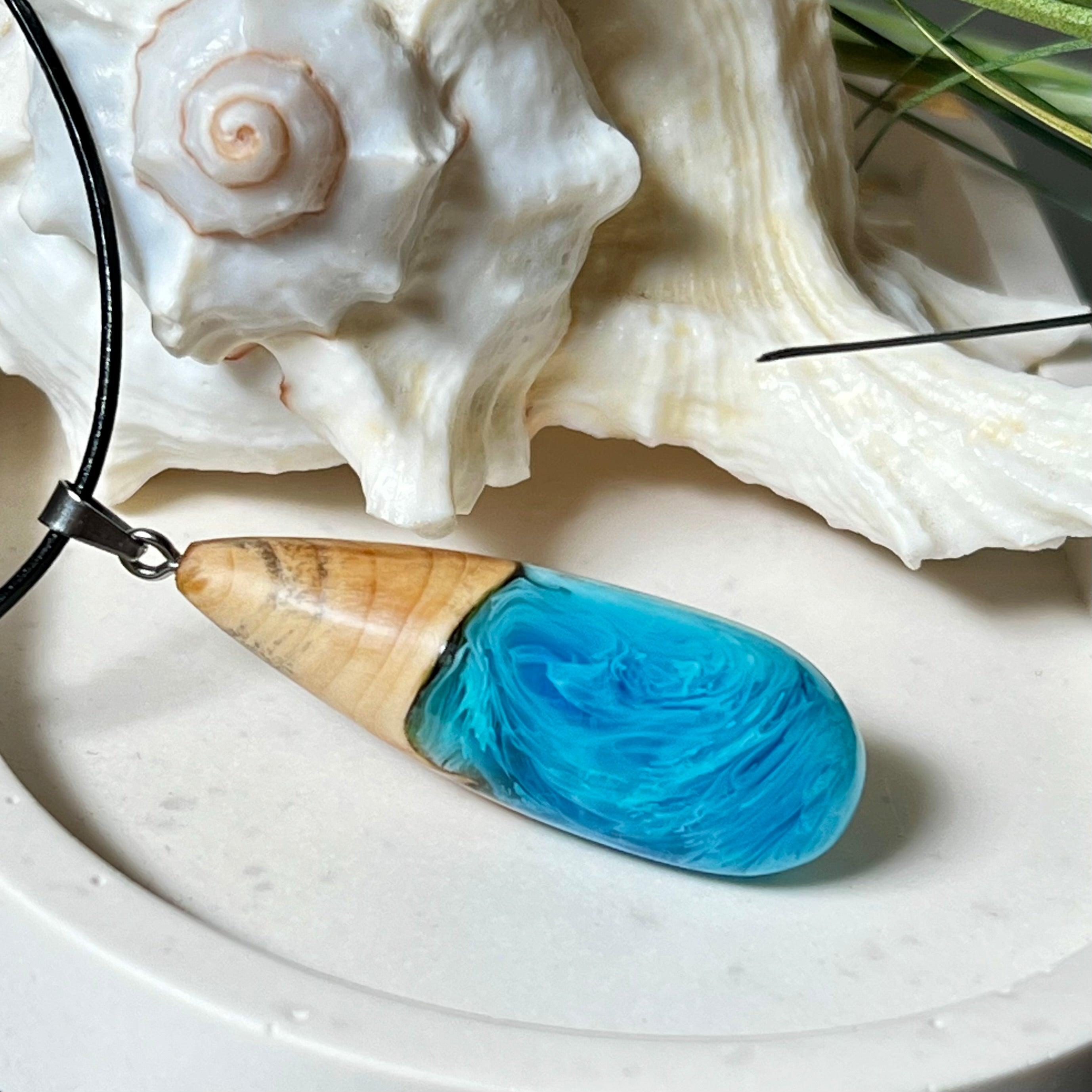 Tropfenförmiger Anhänger aus Maserholz und Harz in leuchtenden Blautönen und Weiß. Inspiriert vom Meer, in Handarbeit gegossen,gesägt, geschliffen und hochglanzpoliert. Mit verstellbarer Lederkette (45 + 5 cm) und Edelstahlkarabiner. Jeder Anhänger ist ein Unikat mit natürlicher Maserung. Ein maritimes Schmuckstück für Naturfreunde und alle, die das Wasser lieben.
