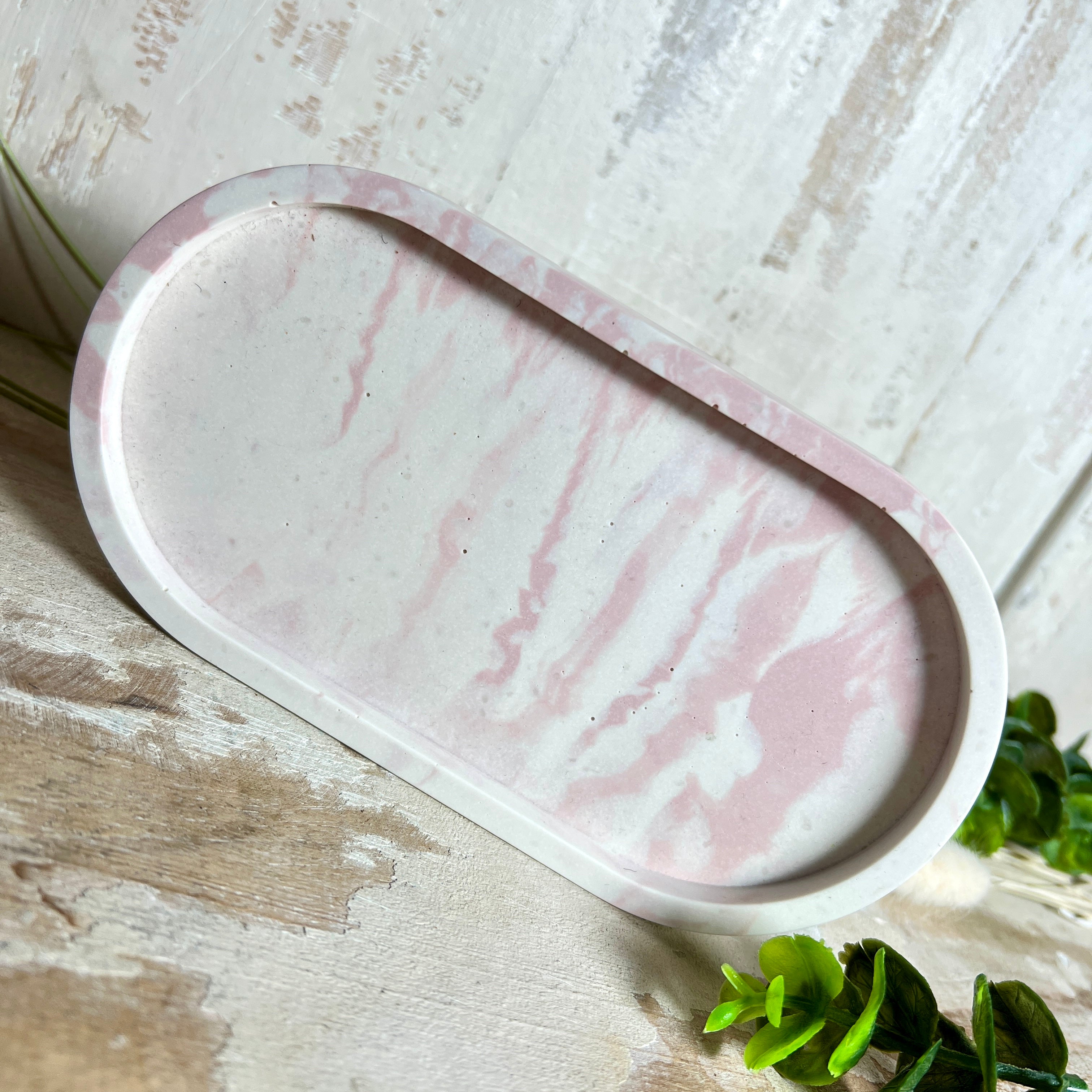 Schmucktablett aus Jesmonite in zartem Rosa-Weiß-Marmor. Handgegossenes, ovales Deko-Tablett mit glatter Oberfläche und Korkfüßen. Perfekt als Ablage für Schmuck, Schlüssel, Brille oder Dekoobjekte. Jedes Stück ein liebevoll gefertigtes Unikat in der Größe 17,5 × 9,5 × 1,7 cm.