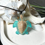 Handgefertigter Schildkröten-Anhänger Turtle Harmony aus echtem Meersand und transparent-türkisfarbenem Harz, kombiniert mit einer kleinen Jaspisperle. Symbol für Weisheit, Schutz und Harmonie. Mit Edelstahl-Anhängerschlaufe und Lederkette (45 + 5 cm). Maritimer Schmuck als Unikat, ideal als liebevolles Geschenk oder stilvolles Accessoire für den Alltag.