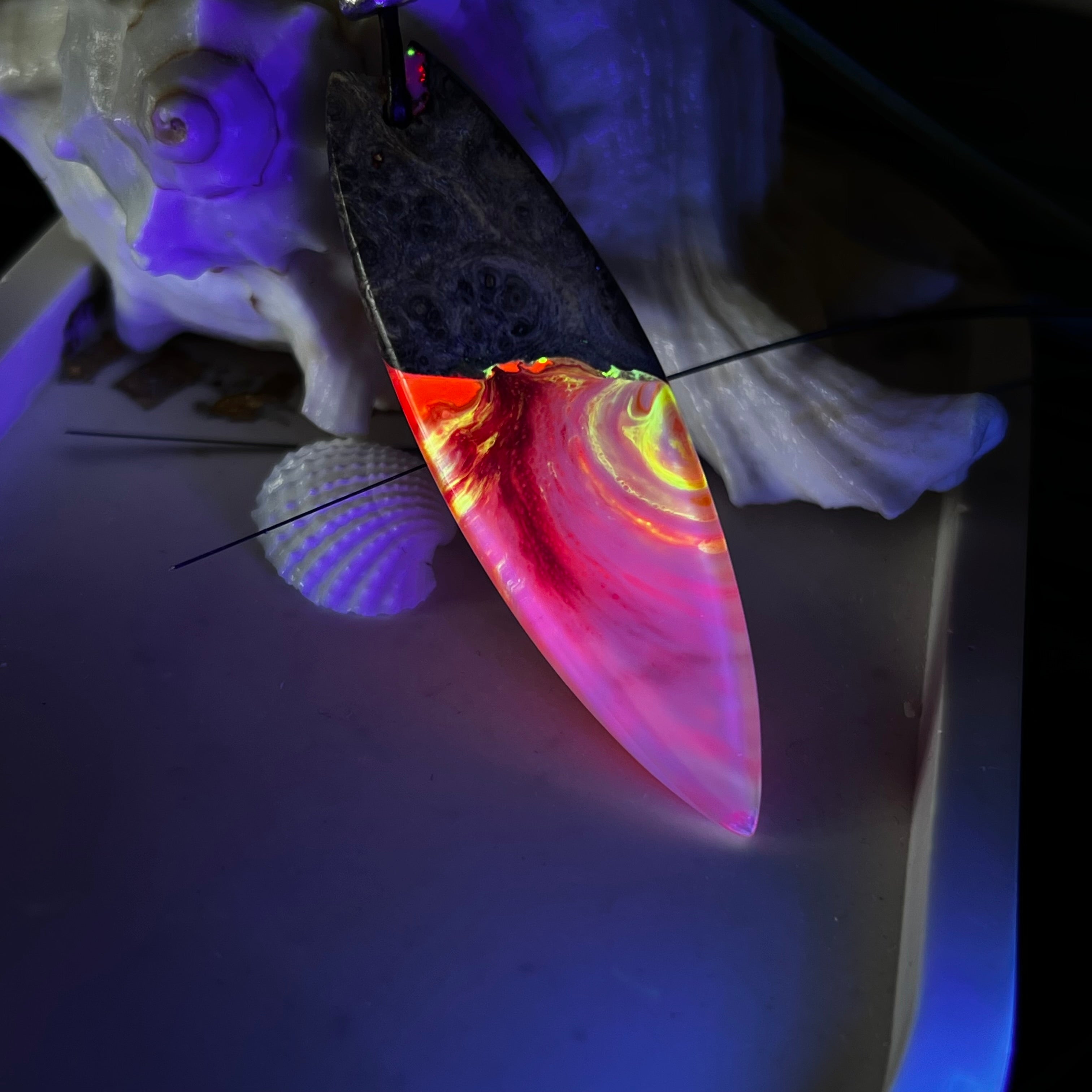 Aurora Flame – fluoreszierender Surfbrett-Anhänger aus Maserholz und leuchtendem Epoxidharz in Rosa, Pink, Orange und Weiß. Der handgefertigte Unikat-Anhänger fluoresziert bei Schwarzlicht in intensiven Farbtönen. Er ist ca. 6,3 x 2 cm groß, wird an einem verstellbaren Lederband (26–45 cm) getragen und ist mit einer silberfarbenen Spacerperle verziert. Ein ausdrucksstarkes Schmuckstück für Menschen mit Persönlichkeit.