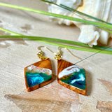 Handgefertigte Ohrringe „Ocean Diamond“ aus Olivenholz und Epoxidharz in Diamantform. Türkis-, Blau- und Weißtöne bilden ein wellenartiges Design, inspiriert vom Meer. Jeder Ohrring ist ein Unikat mit individueller Maserung. Vergoldete, nickelfreie und bleifreie Anhängerschlaufe, 925 Sterling Silber Ohrhaken. Maritimer Schmuck für Meerliebhaber und besondere Anlässe.