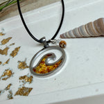 “Runder Wellenanhänger aus Edelstahl mit Bernstein-Harz-Inlay, Jaspisperle & facettiertem Bergkristall an schwarzer Lederkette (45 cm + 5 cm).”