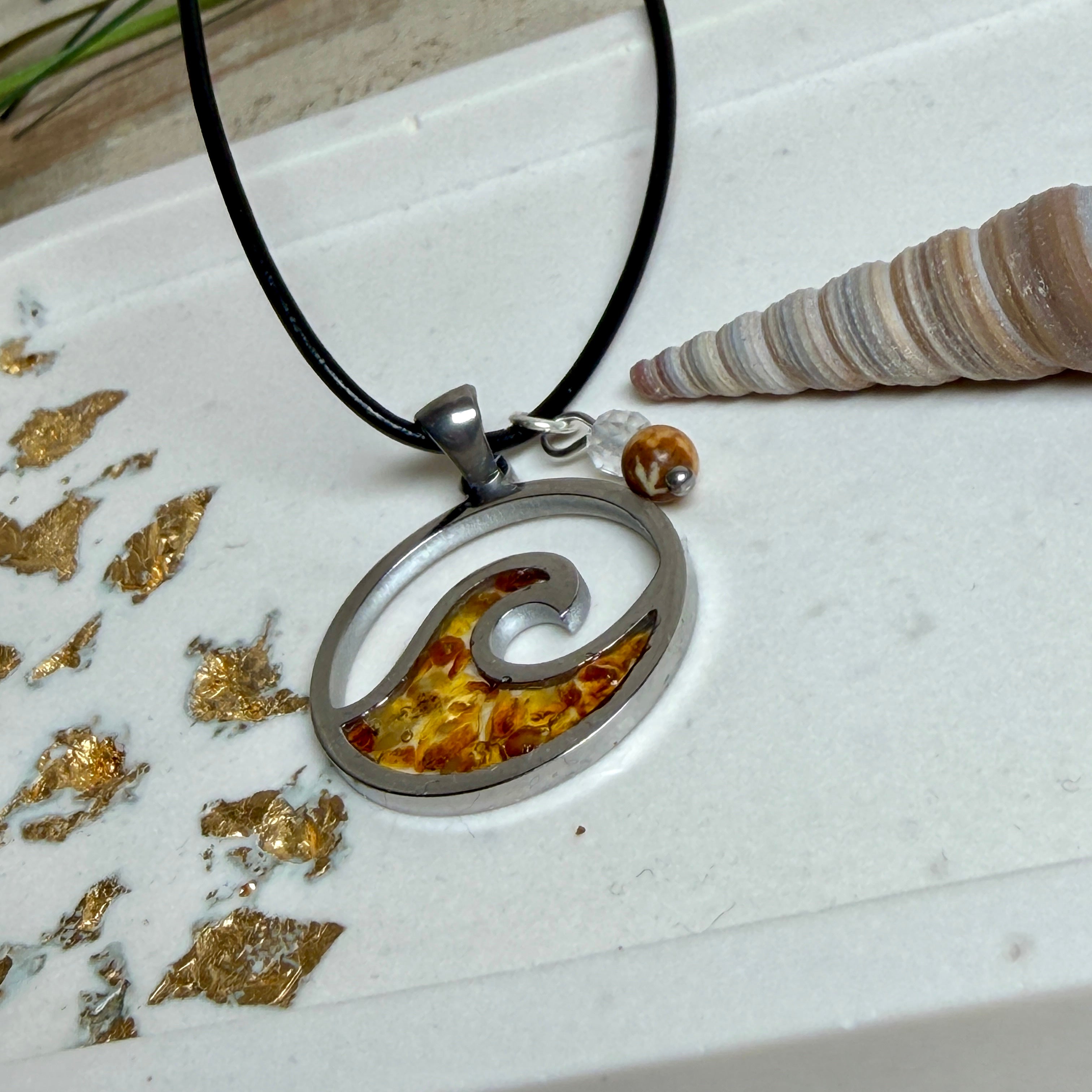 “Runder Wellenanhänger aus Edelstahl mit Bernstein-Harz-Inlay, Jaspisperle & facettiertem Bergkristall an schwarzer Lederkette (45 cm + 5 cm).”