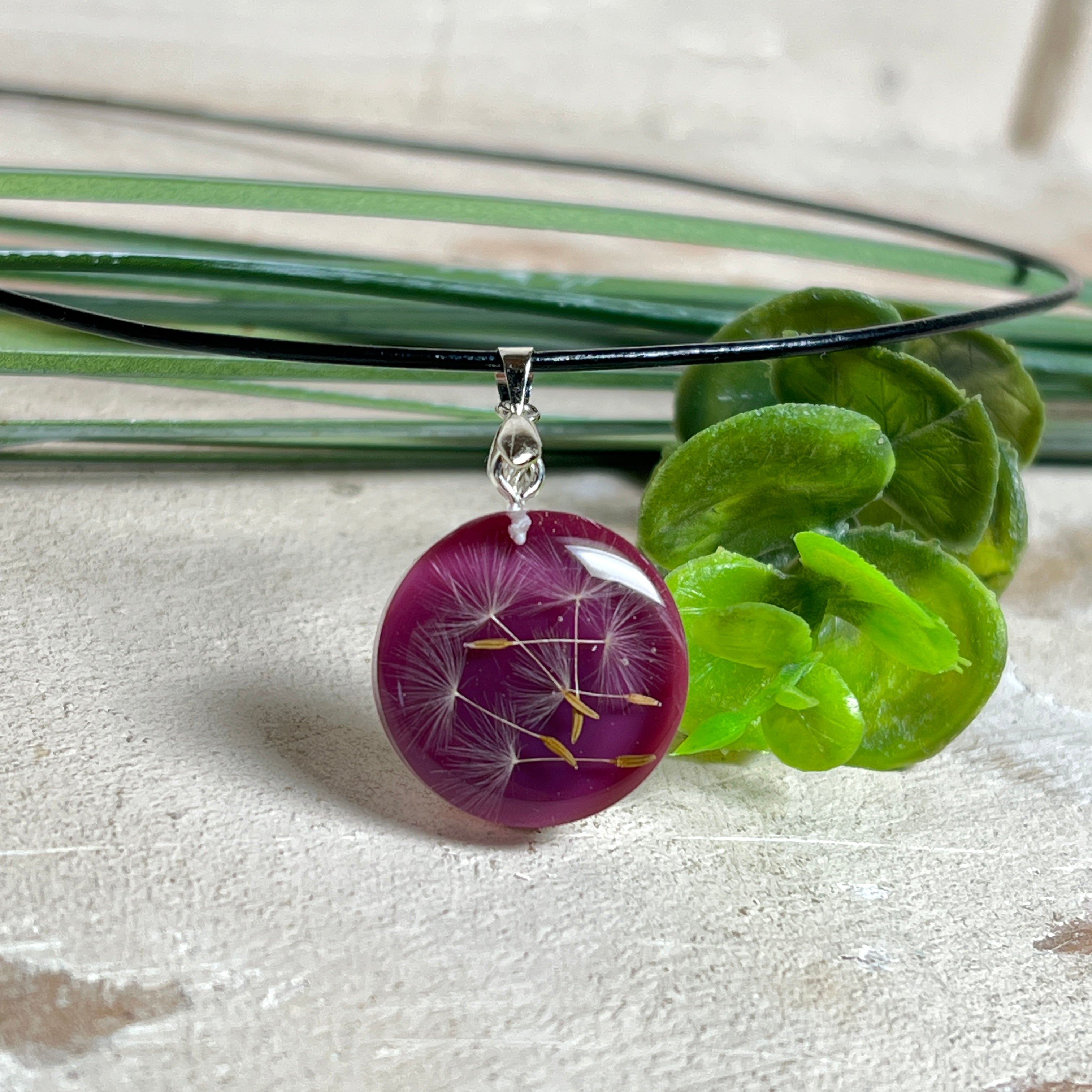 Runder Pusteblumen-Anhänger aus Harz, Hintergrund Brombeerfarben. Durchmesser 22 mm, Edelstahlöse, Lederkette verstellbar mit Edelstahlverschluss.