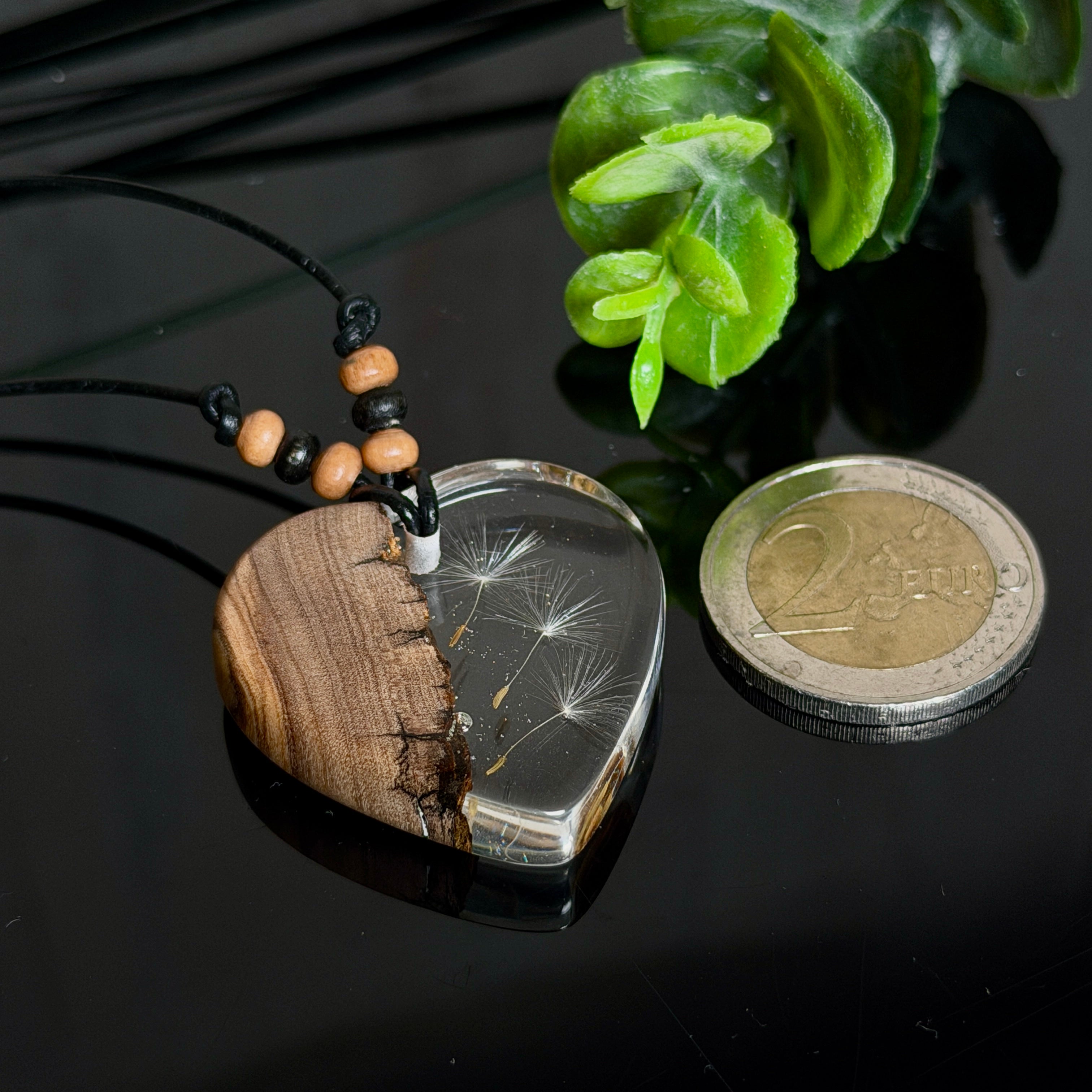Handgefertigter Herzanhänger aus warm gemasertem Olivenholz und kristallklarem Epoxidharz mit schwebenden Pusteblumensamen. Schwarzes, verstellbares Lederband mit Schiebeknoten und naturfarbenen Holzperlen, Anhänger ca. 3,5 × 3,3 cm. Naturnaher Unikatschmuck von ZeitlosSchmuckDesign.