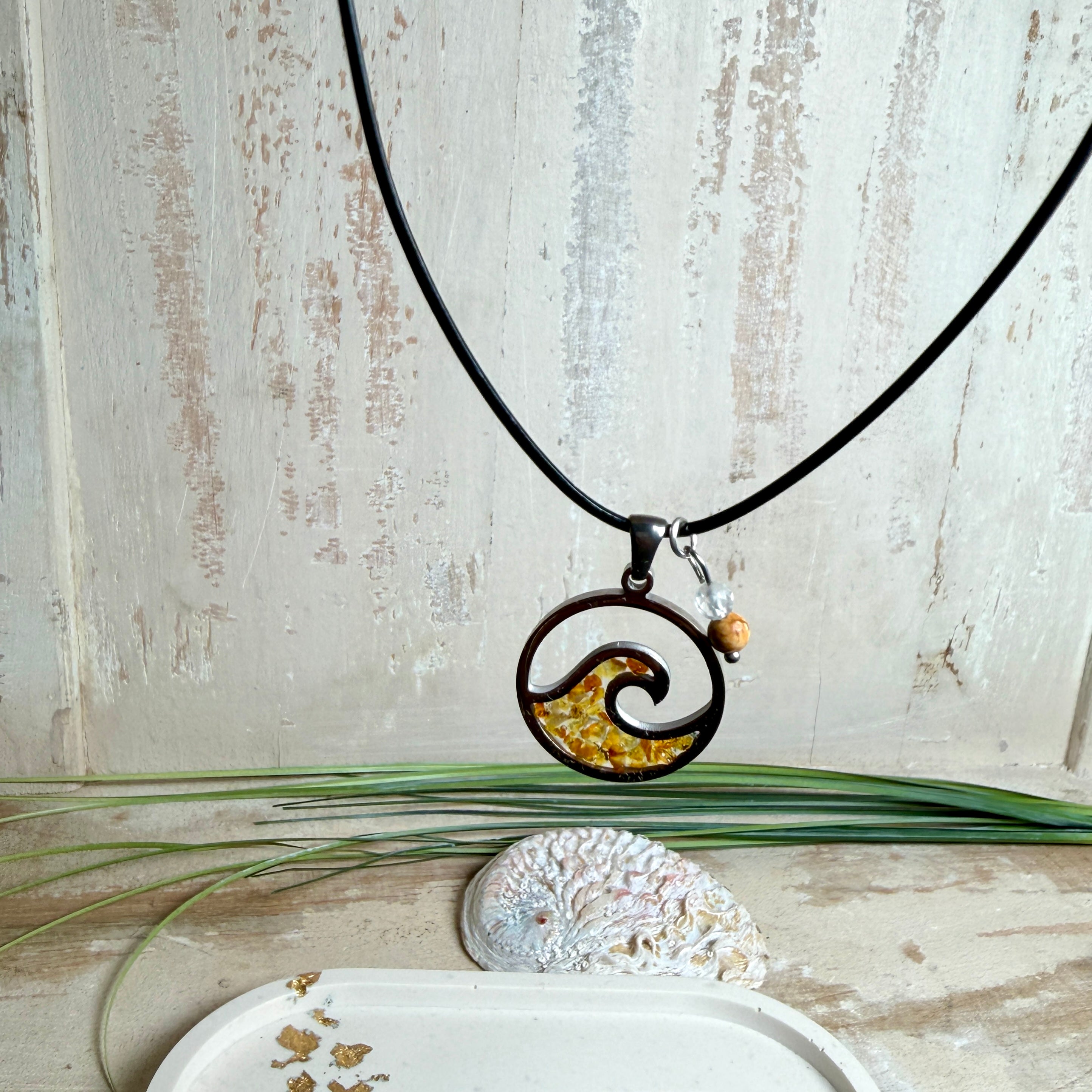 “Runder Wellenanhänger aus Edelstahl mit Bernstein-Harz-Inlay, Jaspisperle & facettiertem Bergkristall an schwarzer Lederkette (45 cm + 5 cm).”