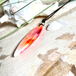 Handgefertigter Surfbrett-Anhänger aus fluoreszierendem Epoxidharz in leuchtenden Orange-, Rot- und Gelbtönen. Leuchtet bei Schwarzlicht. Kombiniert mit verstellbarem Lederband (26–45 cm), verziert mit Spacer- und Holzperlen. Das Design ist inspiriert von der Farbintensität eines Sonnenuntergangs über dem Meer.