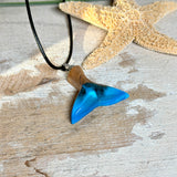 Handgefertigter Walflossen-Anhänger aus Olivenholz und Epoxidharz in Blau-Grün-Weiß, polierte Oberfläche, Edelstahl-Öse. Schwarze Lederkette 45 cm mit Edelstahl-Karabinerverschluss und 5 cm Edelstahl-Verlängerung. Anhängergröße ca. 2,5 × 3,2 cm, maritime Produktfotografie.