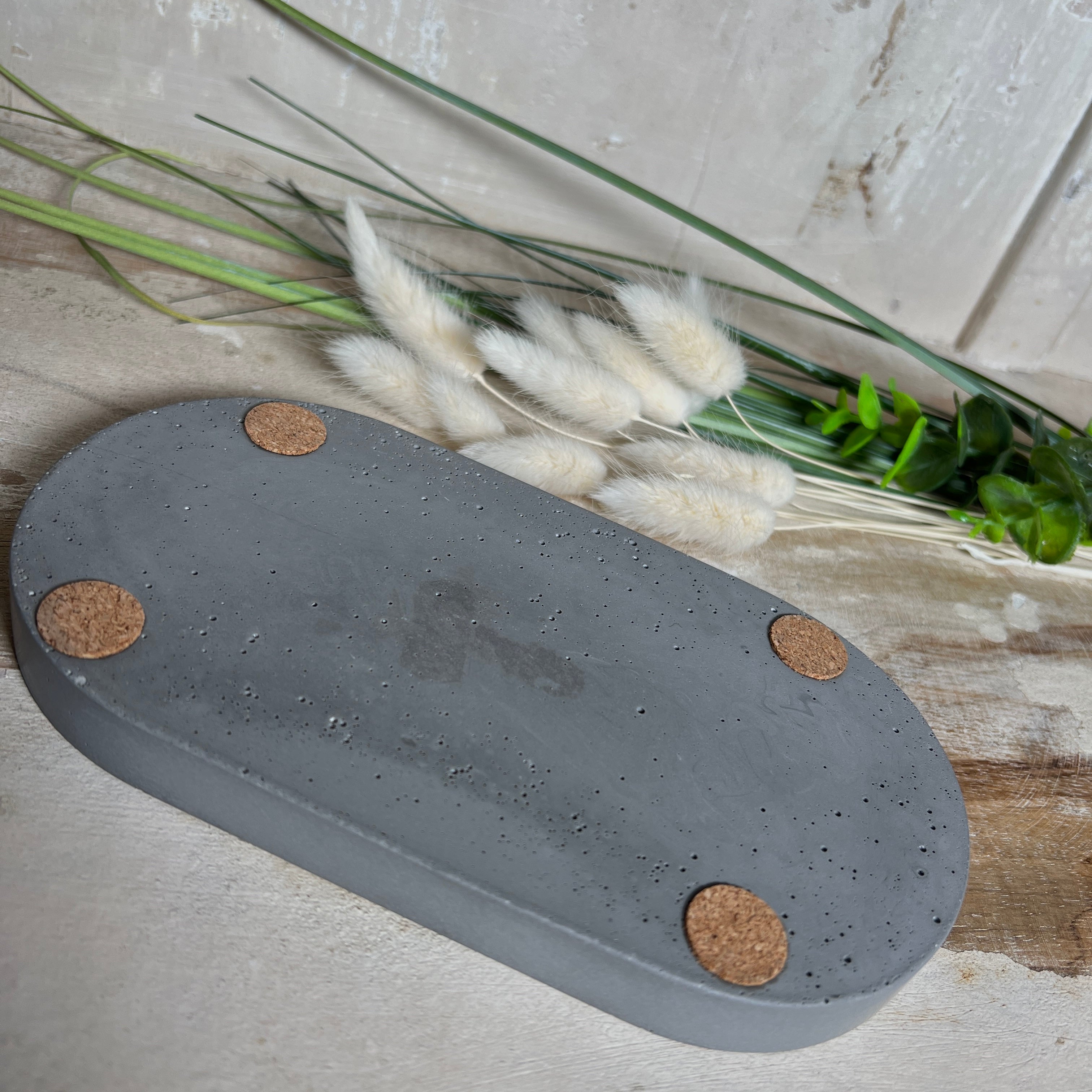 Handgefertigtes ovales Schmucktablett aus grauen  Jesmonite mit schimmernden Blattgold-Details. Die Unterseite ist mit vier Korkpunkten versehen und schützt empfindliche Oberflächen. Ideal zur stilvollen Aufbewahrung von Schmuck, Schlüsseln, Brille oder kleinen Dekoartikeln. Jedes Tablett ist ein Unikat mit individueller Maserung und goldenen Akzenten – Lieferung ohne Deko. Die 