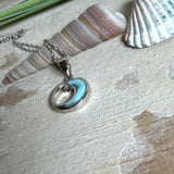 Feine Wellen-Kette aus rhodiniertem 925 Silber. Der runde Anhänger zeigt eine stilisierte Welle mit hellblauem Larimar-Cabochon, eingefasst in poliertem Silber. Größe des Anhängers ca. 23 x 13 mm, an einer 45 cm langen, 1 mm starken, rhodinierten Silberkette. 