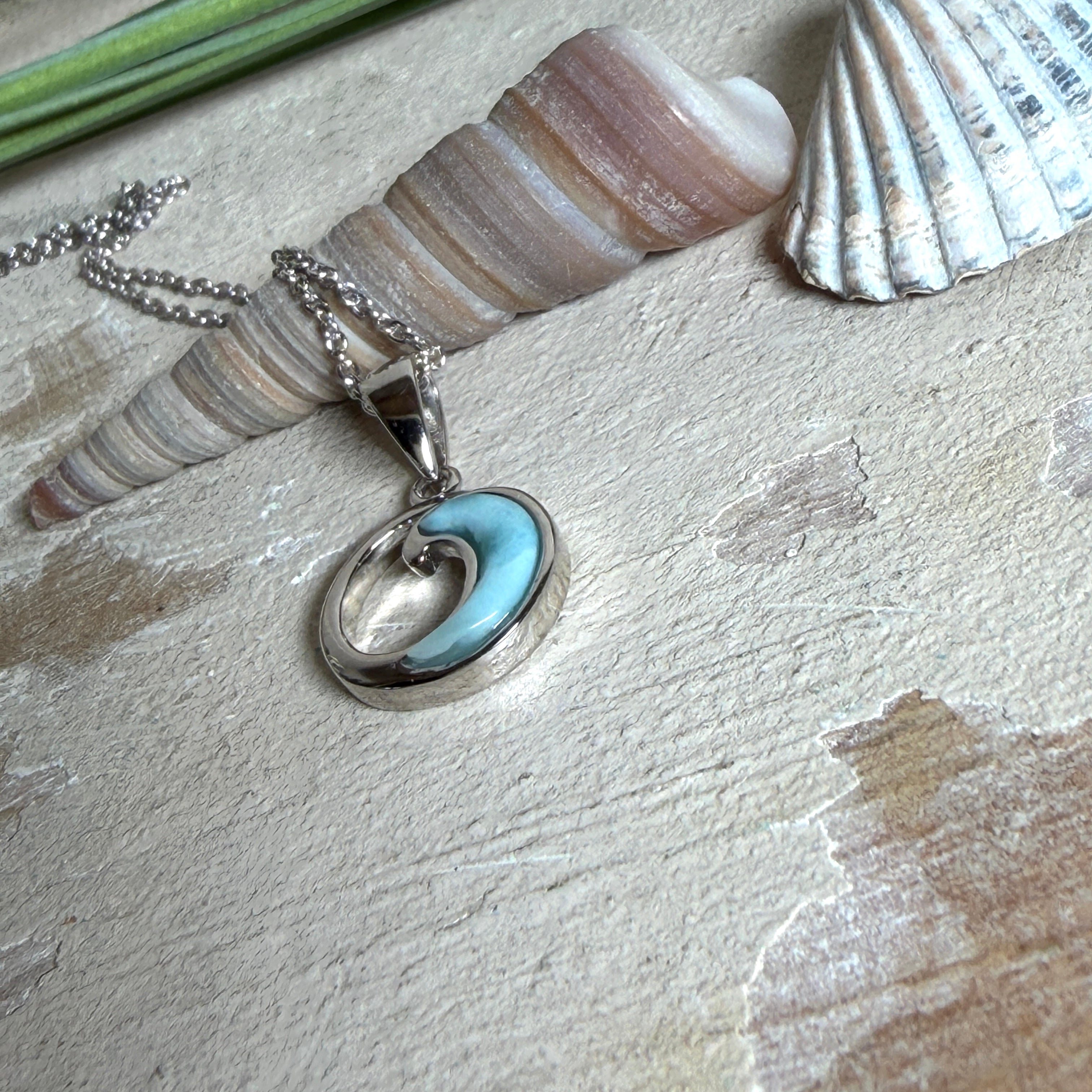 Feine Wellen-Kette aus rhodiniertem 925 Silber. Der runde Anhänger zeigt eine stilisierte Welle mit hellblauem Larimar-Cabochon, eingefasst in poliertem Silber. Größe des Anhängers ca. 23 x 13 mm, an einer 45 cm langen, 1 mm starken, rhodinierten Silberkette. 