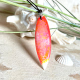 Handgefertigter Surfbrett-Anhänger aus fluoreszierendem Epoxidharz in leuchtenden Orange-, Rot- und Gelbtönen. Leuchtet bei Schwarzlicht. Kombiniert mit verstellbarem Lederband (26–45 cm), verziert mit Spacer- und Holzperlen. Das Design ist inspiriert von der Farbintensität eines Sonnenuntergangs über dem Meer.