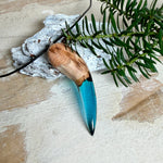 Handgefertigter Anhänger aus Edelholz und transparent-türkisblauem Epoxidharz, glatt poliert. Größe ca. 6,7 × 2,0 cm. Mit Edelstahlöse an schwarzer Lederkette (45 cm + 5 cm Edelstahl-Verlängerung, Karabiner). Maritimer, moderner Unisex-Schmuck mit natürlicher Holzmaserung; kleine Lufteinschlüsse sind charakteristisch.