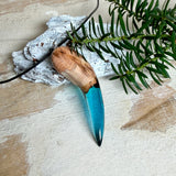 Handgefertigter Anhänger aus Edelholz und transparent-türkisblauem Epoxidharz, glatt poliert. Größe ca. 6,7 × 2,0 cm. Mit Edelstahlöse an schwarzer Lederkette (45 cm + 5 cm Edelstahl-Verlängerung, Karabiner). Maritimer, moderner Unisex-Schmuck mit natürlicher Holzmaserung; kleine Lufteinschlüsse sind charakteristisch.
