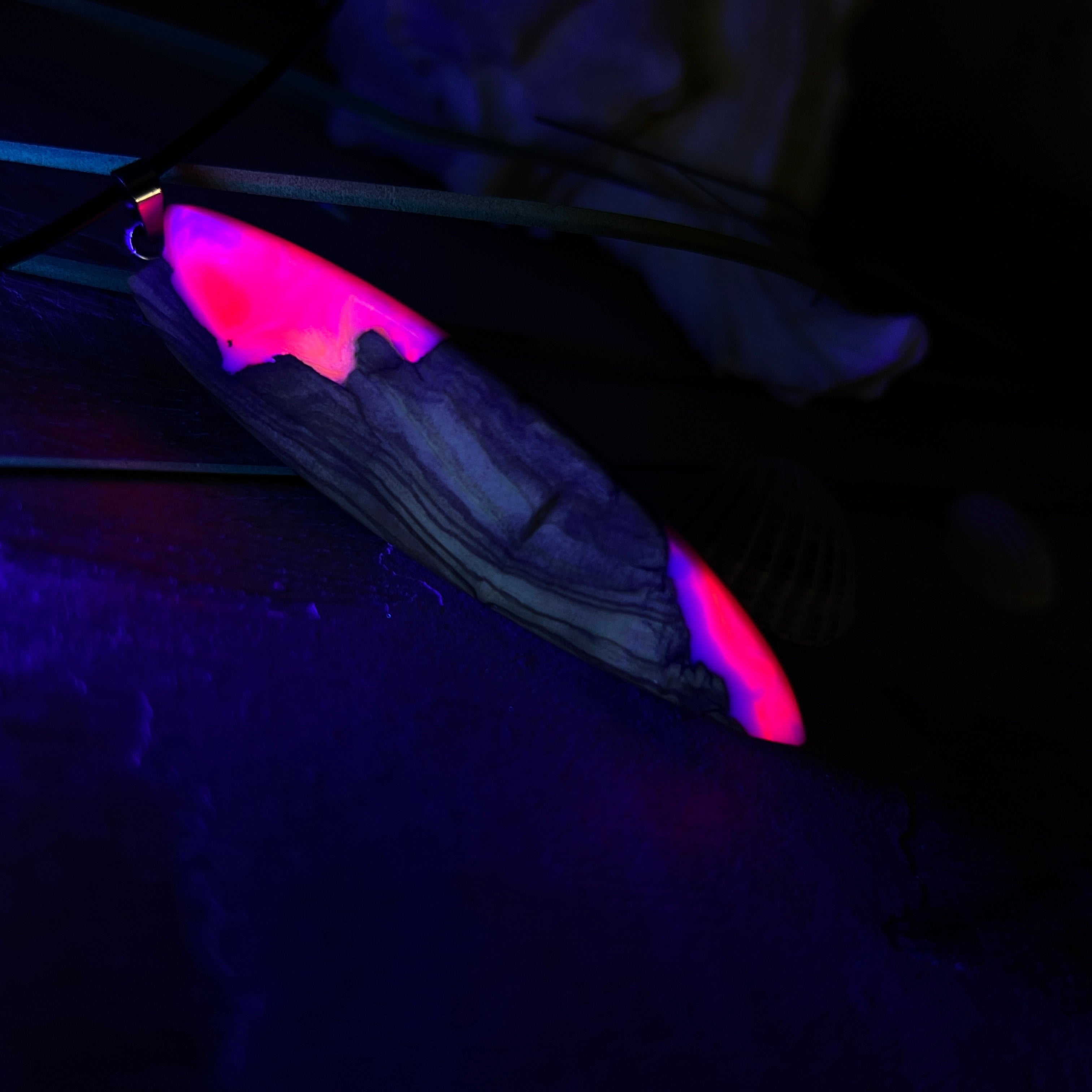 Handgefertigter Surfbrett-Anhänger „Pink Glow“ aus edlem Olivenholz und fluoreszierendem Epoxidharz in Pink & Weiß. Fluoreszierend bei Schwarzlicht, mit Edelstahl-Anhängerschlaufe und schwarzer Lederkette (45 cm + 5 cm Verlängerung). Ein maritimes Unikat – perfekt als Geschenk für Surfer und Meeresliebhaber.