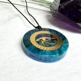 Runder Anhänger mit goldenem Horusauge aus Metall in blau türkis violettem Epoxidharz am schwarzen Baumwollband, spiritueller Eye of Ra Naturschmuck Amulett